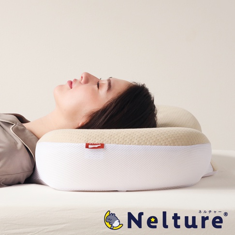 一位女子側臥，頭部置於 NELUD 完美釋壓Q彈棉花糖枕上。枕頭為米白色與淺黃色拼接設計，外層為網狀織物材質，表面有紅色品牌標籤。