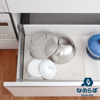 銀色金屬濾網、不鏽鋼盆、白色鍋蓋置於淺色珪藻土墊上，旁邊有一個藍色鍋。