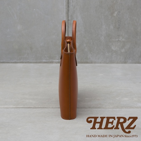 側邊視角展示一個棕色皮革公事包，包身薄型，有兩個圓形提把，開口處有金屬釦，包體縫線整齊。