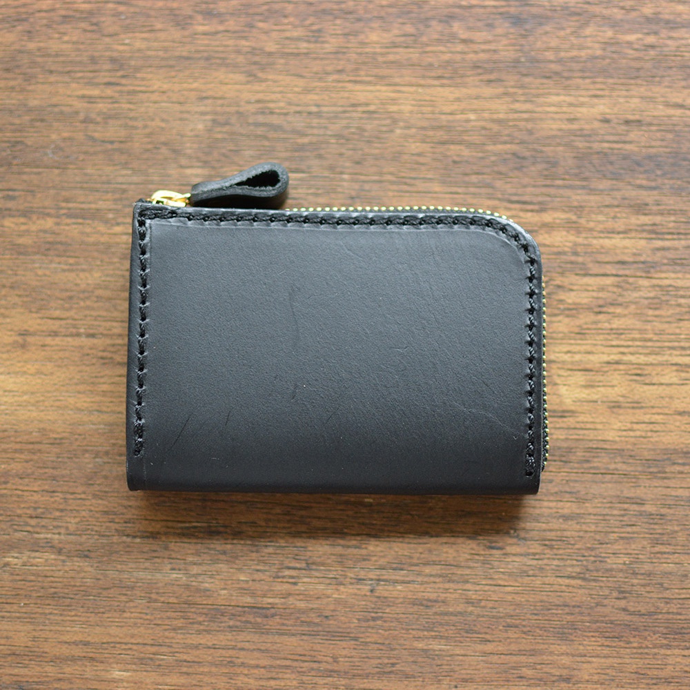 黑色皮革拉鍊短夾，附有金屬拉鍊及皮革拉頭，邊緣有縫線裝飾，置於木質桌面。