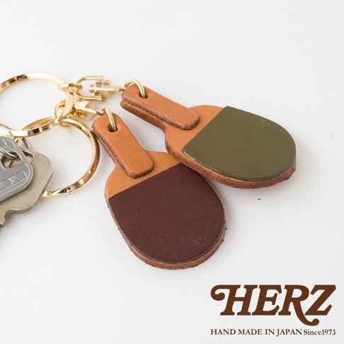 職人手作皮革桌球拍造型鑰匙圈，由淺棕色和深棕色皮革拼接而成，搭配金色金屬掛環和鑰匙。