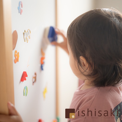 木製兒童多功能繪畫白板，白色板面貼有彩色動物、字母磁貼，一名兒童正使用藍色擦拭板擦拭。