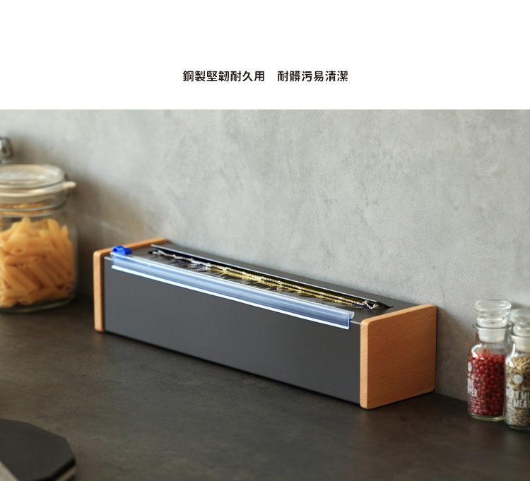 日本製原木鋼製保鮮膜切割器，深灰色鋼製外殼搭配淺木色木製側邊，頂部有透明壓克力切割條及藍色滑塊，內含保鮮膜。