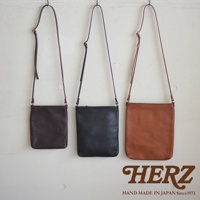 三款職人手作皮革Organ肩背小方包，分別為深棕色、黑色與棕色，皆為簡約方形設計，搭配細長皮革背帶，懸掛於白色牆面上。