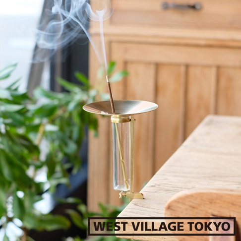 黃銅可夾式玻璃線香架，帶有一個圓形黃銅接灰盤，盤下為透明玻璃管，管內有一根細黃銅桿，上方插著燃燒的線香，散發出白色煙霧。