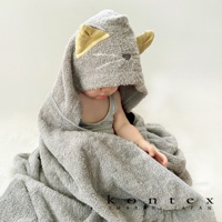 今治純棉Q萌貓耳連帽浴巾，採用柔軟親膚的純棉材質，此款為灰色，連帽處設計有可愛的貓耳朵，耳朵內側為黃色條紋，浴巾包裹著一個嬰兒，營造溫馨可愛的氛圍。