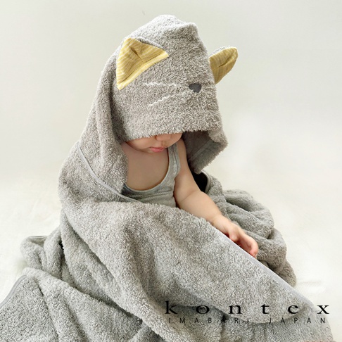 今治純棉Q萌貓耳連帽浴巾，採用柔軟親膚的純棉材質，此款為灰色，連帽處設計有可愛的貓耳朵，耳朵內側為黃色條紋，浴巾包裹著一個嬰兒，營造溫馨可愛的氛圍。