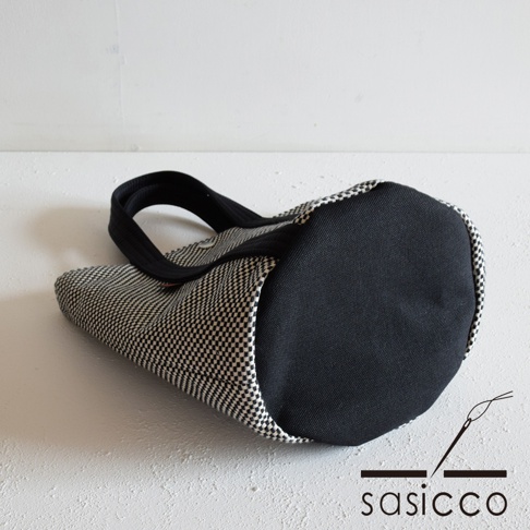 三河木綿刺子織兩用水桶包，採用黑白格紋刺子織布料，搭配黑色素面底部和提把，呈現簡約設計。