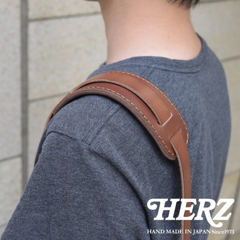 職人手作皮革肩墊，淺棕色皮革，附有縫線細節，實際佩戴在灰色T恤的肩膀上。