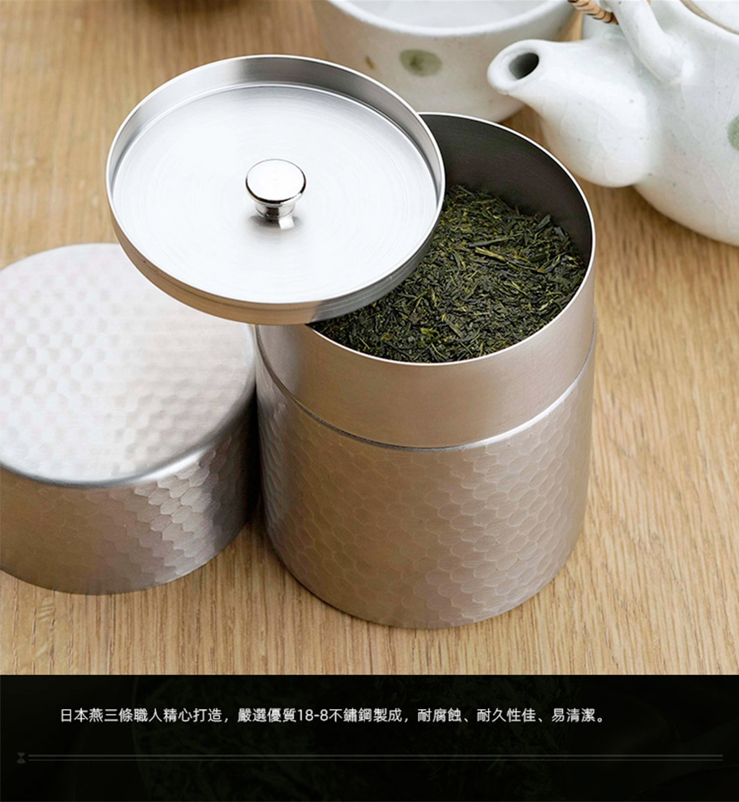 日製18-8不鏽鋼錘目紋茶葉罐，罐身有著細緻的錘打紋理，銀色金屬質感，罐內裝有綠色茶葉，附有同材質的圓形蓋子，蓋子中央有小提把。