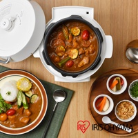 白色電子壓力鍋，鍋內盛有咖哩，配料有雞肉、櫛瓜、小番茄、秋葵等。旁邊另有一盤咖哩飯，飯旁有玉米、秋葵、小番茄、生菜沙拉。另有木盤盛裝醃漬小菜與炸洋蔥。