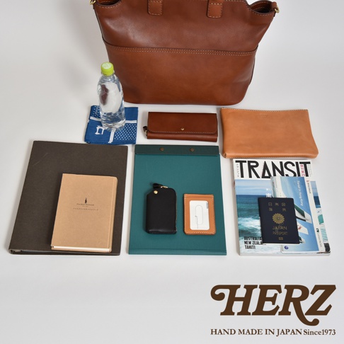 職人手作皮革大容量兩用托特包 T-8，展示多種配件：棕色皮革托特包、水瓶、藍色印花布、咖啡色皮夾、淺棕色化妝包、黑色手機包、咖啡色卡夾、筆記本、綠色文件夾及旅遊雜誌、護照。