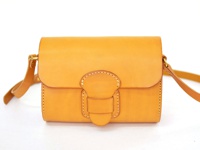 淺棕色皮革馬鞍包，有寬版皮帶和獨特的皮革搭扣設計，車縫線清晰可見，整體呈現簡約風格。