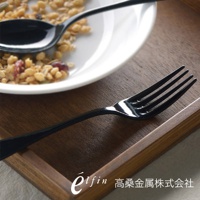 黑色琺瑯餐叉，四齒設計，光滑表面，搭配白色餐盤與麥片，置於木質托盤上。