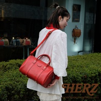 紅色皮革職人手作波士頓包，可肩背或手提，包身有拉鍊開合，配有可調整長度的皮革肩帶，包身結構紮實，品牌標誌壓印於正面中央。