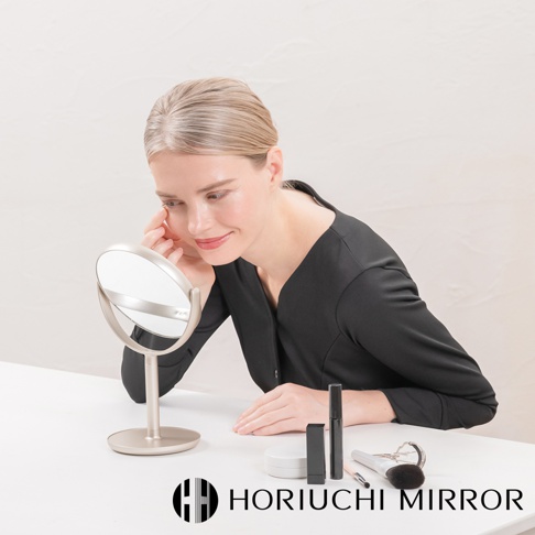 香檳金色桌上型化妝圓鏡，鏡面可旋轉，旁有睫毛膏、粉撲和化妝刷。