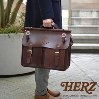 職人手作皮革旅行包 A-102，深棕色，正面有兩個翻蓋口袋，搭配金色釦環和皮帶。