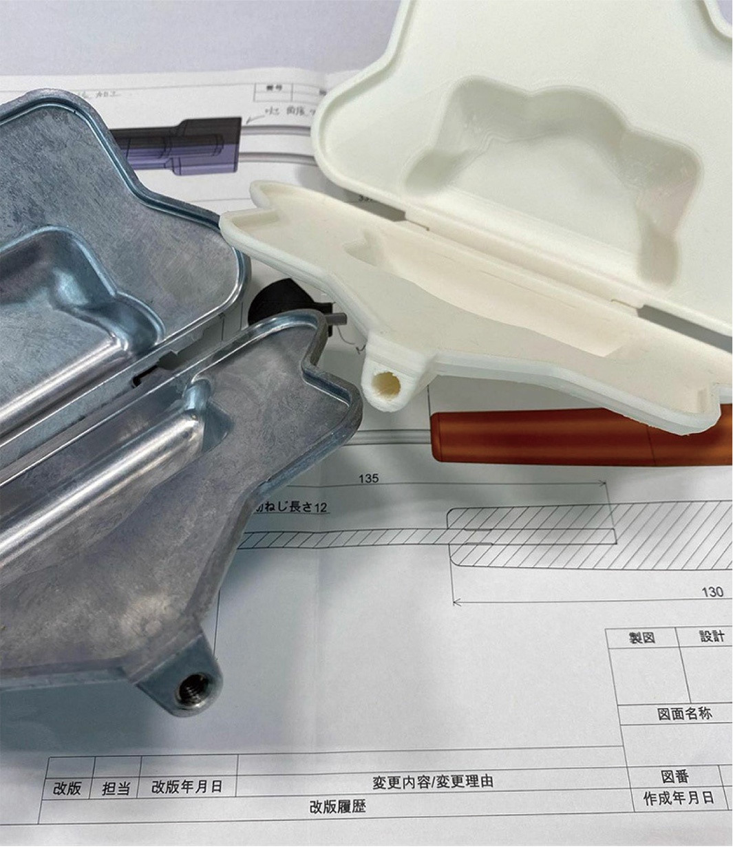 銀色金屬熱壓三明治烤夾與白色塑膠烤夾對比，置於工程圖紙之上，部分區域可見螺絲孔及尺寸標示。