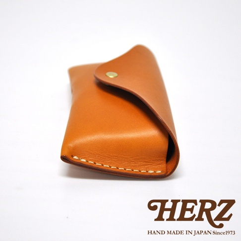 職人手作皮革眼鏡收納盒，附有金色按扣，皮革呈現溫暖的棕褐色，縫線細緻。