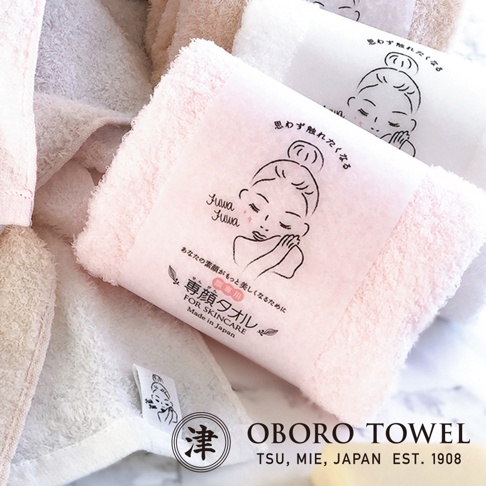 粉色與白色的日本OBORO TOWEL專用洗臉毛巾，毛巾中央包覆著帶有日系手繪女性插畫的粉色紙帶，上方印有Fuwa Fuwa字樣，整體呈現簡約質感，左下角可見毛巾上的標籤細節，底部標示著日本製造與品牌資訊。