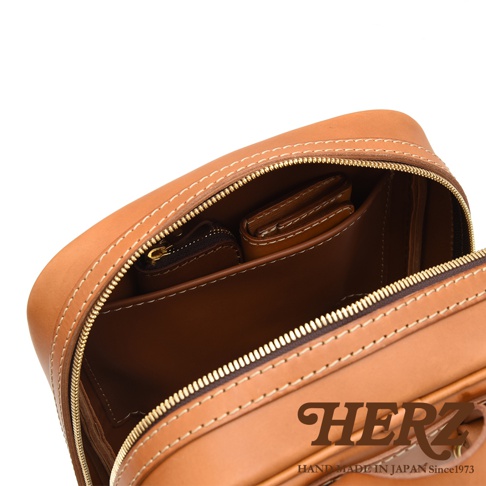 職人手作皮革後背包，展示內部隔層，包含一個拉鍊小袋和一個錢包，材質為棕色皮革，車縫線為米白色。