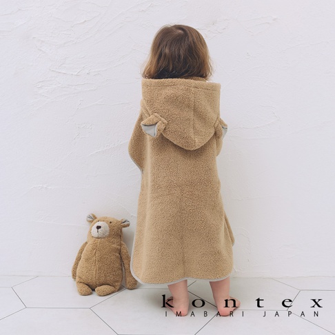 身穿棕色絨毛材質、帶有可愛熊耳朵帽子的斗篷式連帽浴巾的幼童，浴巾邊緣有灰色滾邊。