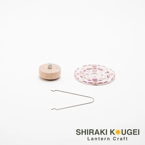 木製燈座，上方有銀色金屬頂飾。旁邊是捲起的白色圓形提燈，印有粉紅色碎花圖案。底部有一對銀色金屬夾子。