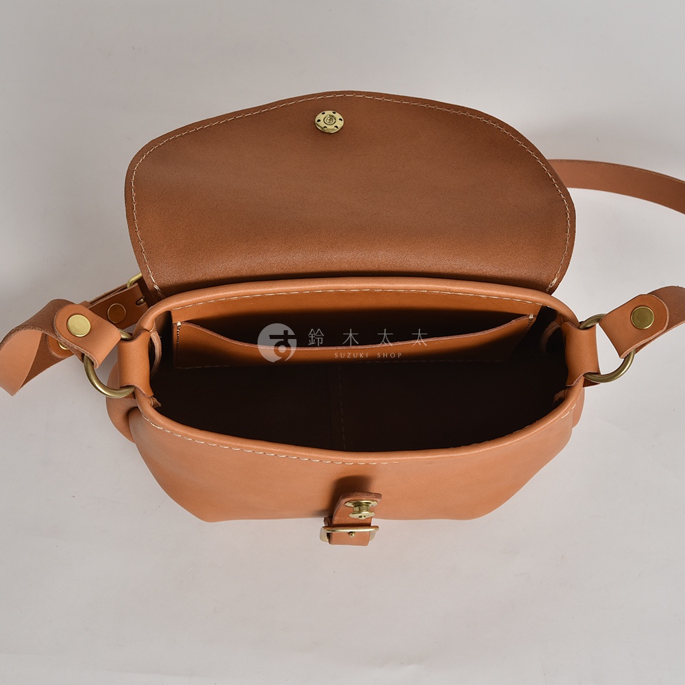 日本HERZ職人手作Stare皮革休閒旅行馬鞍包，棕色翻蓋設計，內有隔層，露出品牌SUZUKI SHOP的標誌。