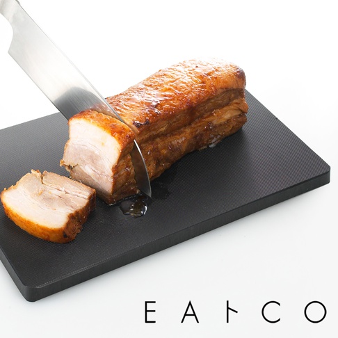 黑色防滑紋理砧板，上面擺放著一塊正在被銀色刀具切割的烤肉。