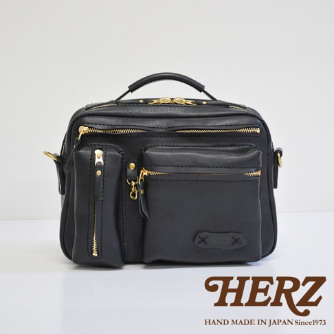 黑色皮革手提斜肩兩用包，包身有多個拉鍊口袋，金色拉鍊與金屬配件，頂部有提把，側面有肩帶掛環，品牌標誌壓印於前袋下方。