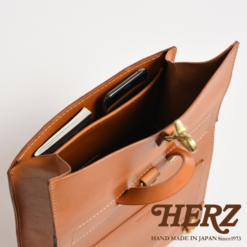 職人手作皮革紙袋風後背包，展示內部隔層，可見手機與護照，材質為棕色皮革，縫線清晰，配有金屬扣環與提把。