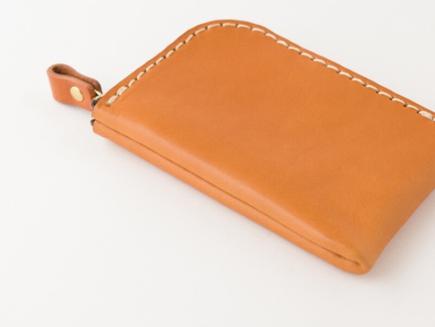 職人手作皮革迷你錢包，採用淺棕色牛皮製成，縫線為米白色。錢包設計簡潔，帶有金色拉鍊和一個皮革拉袢，整體呈現質感。