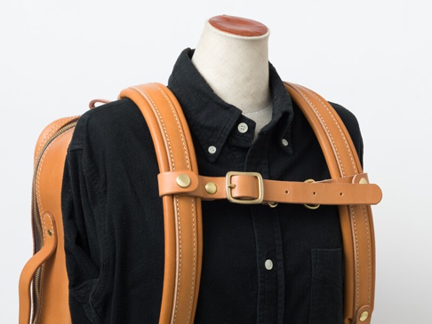 職人手作皮革背包用減壓胸前扣帶，採用天然棕色皮革製成，配有黃銅色金屬扣環和铆釘，用於固定背包肩帶。