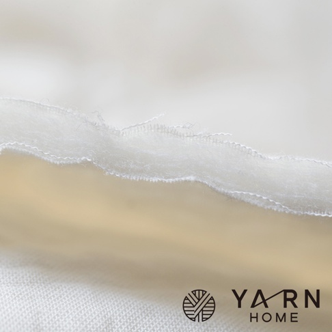 一張極近距離的產品局部特寫鏡頭，呈現出 YARN HOME 紗布巾的多層次結構，展示了由紗布外層包覆脫脂棉填充的柔軟與蓬鬆質感，邊緣車縫線細膩整齊，白色布料表面紋理清晰，角落處印有 YARN HOME 的品牌標誌。