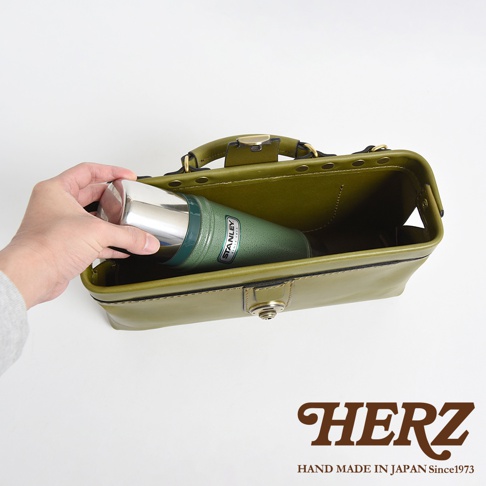 一手拿著綠色Stanley保溫瓶，放入日本HERZ品牌手工製作的橄欖綠皮革橫長形包包內