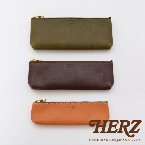 三款職人手作皮革收納筆袋，分別為深綠色、深棕色及橘棕色，皆採用天然皮革材質，配有金色拉鍊和手工縫線，筆袋上有品牌標誌。