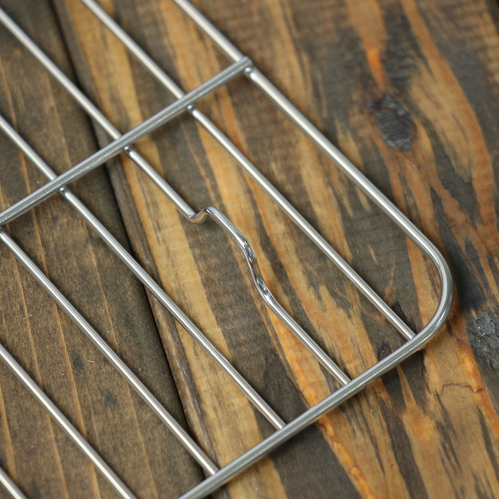 方形不鏽鋼瀝油架，銀色金屬材質，由多條平行細長金屬桿和較粗的金屬邊框組成，表面光滑，架設在深棕色木紋背景上。