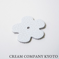 淺灰色皮革製成的花朵形狀吊飾，帶有紋理和中央小孔。