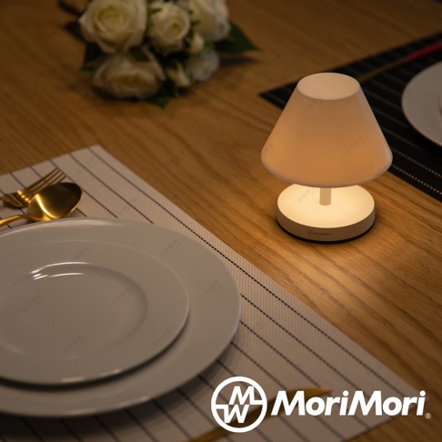 白色傘型LED T-Light CAFE燈，圓形底座，擺放在木質桌面，搭配餐盤與金色餐具。