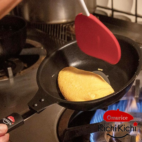 Kichi Kichi 日式神級煎鍋，黑色，用於烹飪金黃色歐姆蛋，鍋柄上有白色與紅色標誌，鍋子置於爐火上。