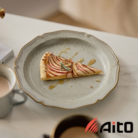 Aito Stitch 美濃燒金彩浮雕經典餐盤上放著一塊蘋果派，派上淋有蜂蜜，灑上開心果碎，旁邊還有咖啡杯。