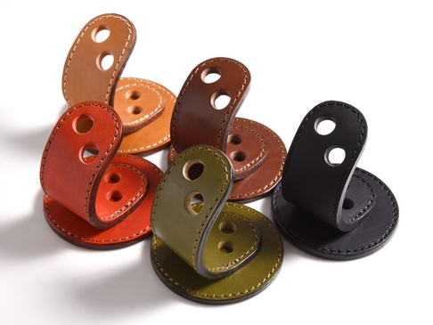 多款職人手作皮革兩入用筆架，顏色包含咖啡色、橘紅色、墨綠色及黑色。每個筆架由兩片皮革組成，下片為圓形底座，上片為彎曲狀，帶有兩個圓孔，整體以縫線裝飾。