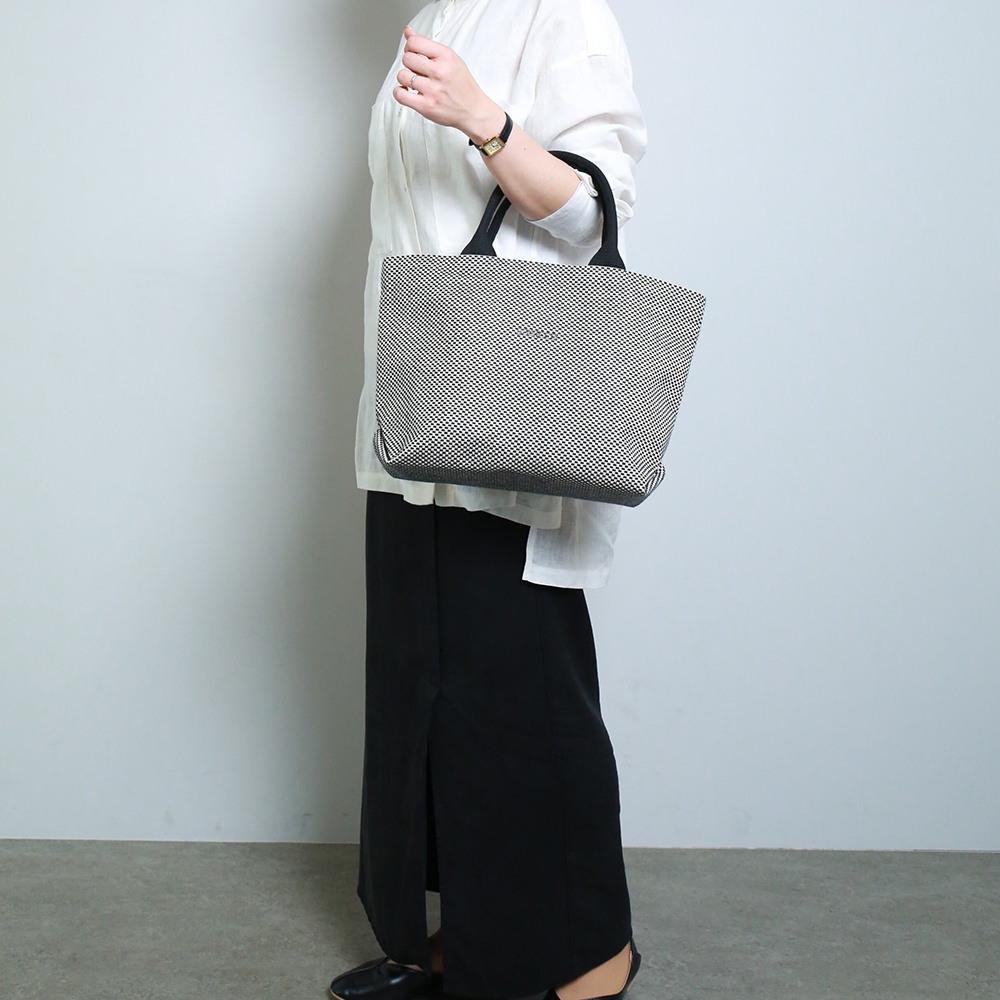 一位女士手提一個三河木綿刺子織經典托特包，包身為黑白格紋圖案，提把為黑色。