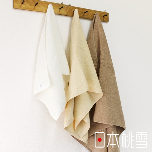 展示三條居家毛巾，分別為白色、淺米色和淺棕色，皆為柔軟材質，掛在木製掛鉤上。