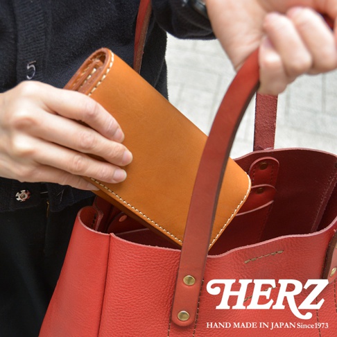 職人手作皮革軟皮長夾 WL-63，展示為琥珀色皮革，搭配紅色皮革手提包，皮革表面有細緻縫線。