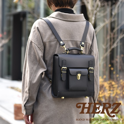 黑色皮革迷你後背包，學院風格設計，配有金屬鎖扣和搭扣，頂部有提把，背帶可調節。