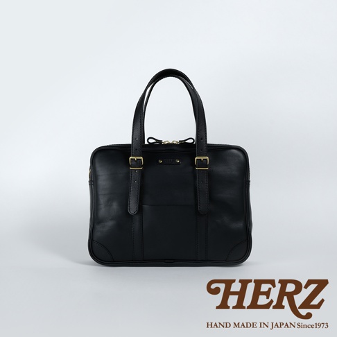 黑色皮革製成的職人手作公事包，可肩背或手提，設有兩個提把、可調節的肩帶扣環，正面有一個開放式口袋和拉鍊開合。