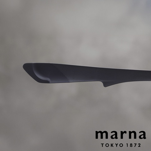 marna TOKYO 1872 標誌旁，黑色多功能食物夾的近景，展示其細長的形狀和優雅的曲線。