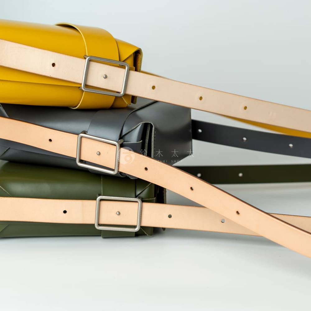 堆疊的黃色、深灰色和軍綠色斜背包，皆配有皮革背帶和金屬扣環