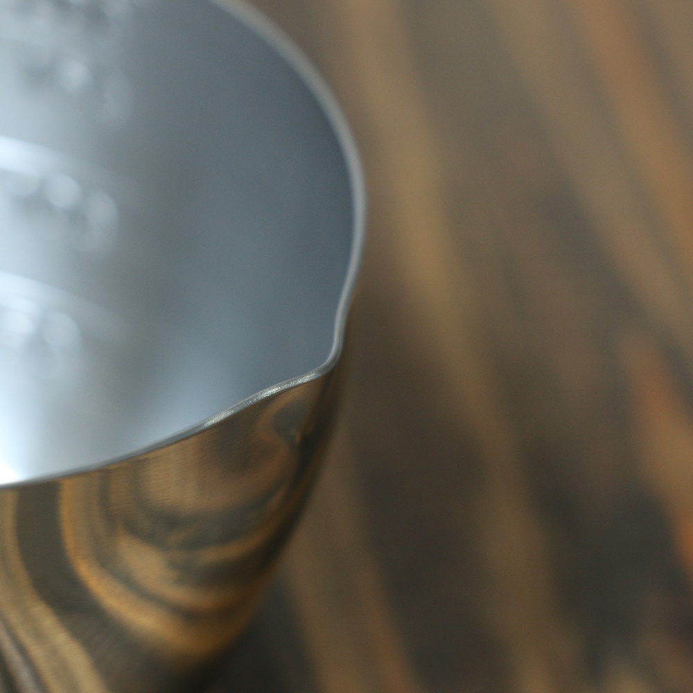 不鏽鋼量杯特寫，顯示其邊緣傾斜的設計與內部的刻度標記，材質呈現金屬光澤。